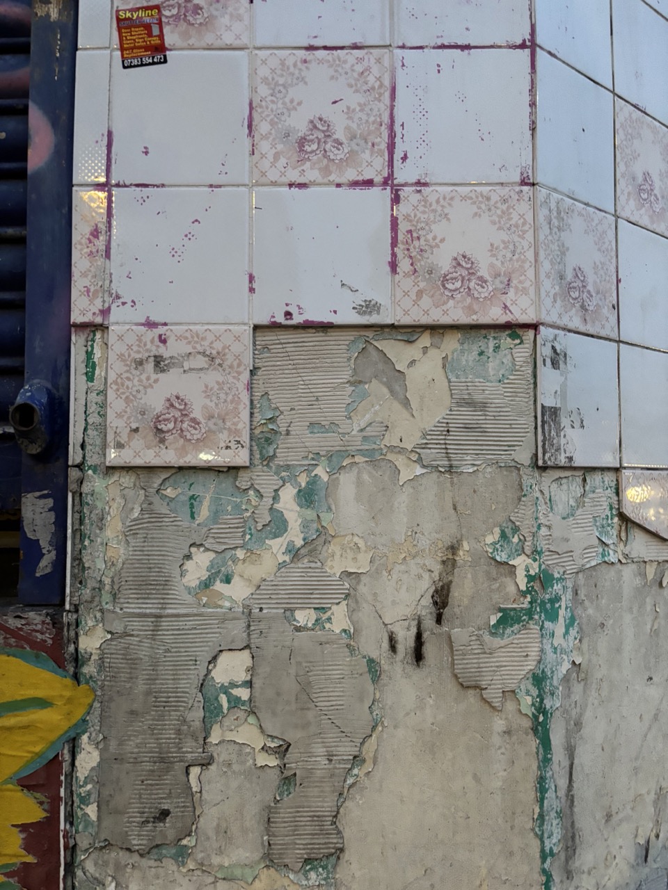 Photograph of building exterior with layers of broken tiles, roller shutter frame